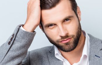 A confident handsome businessman combing his thick dark hair with his fingers.