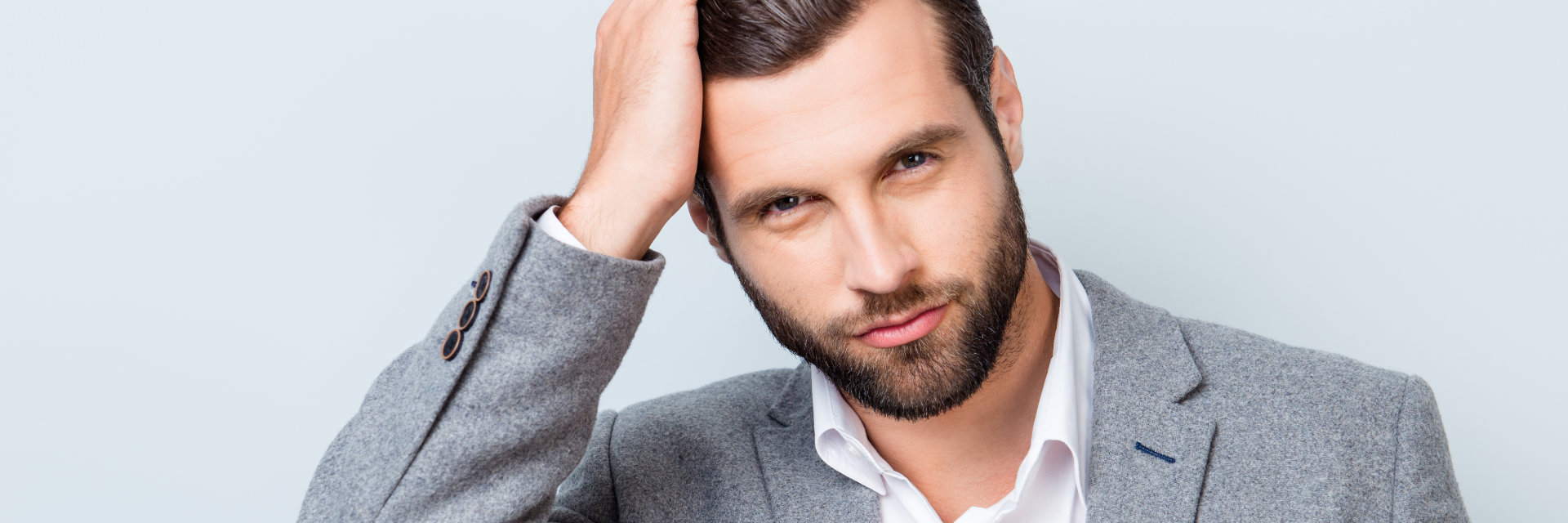 A confident handsome businessman combing his thick dark hair with his fingers.