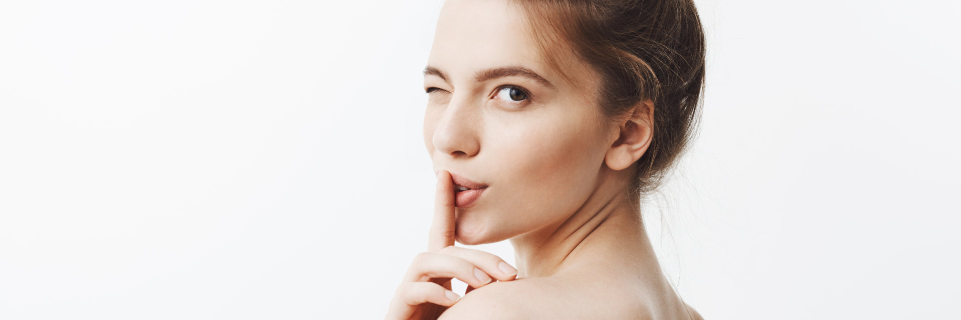 A young woman blinking an eye and putting a finger to her lips.